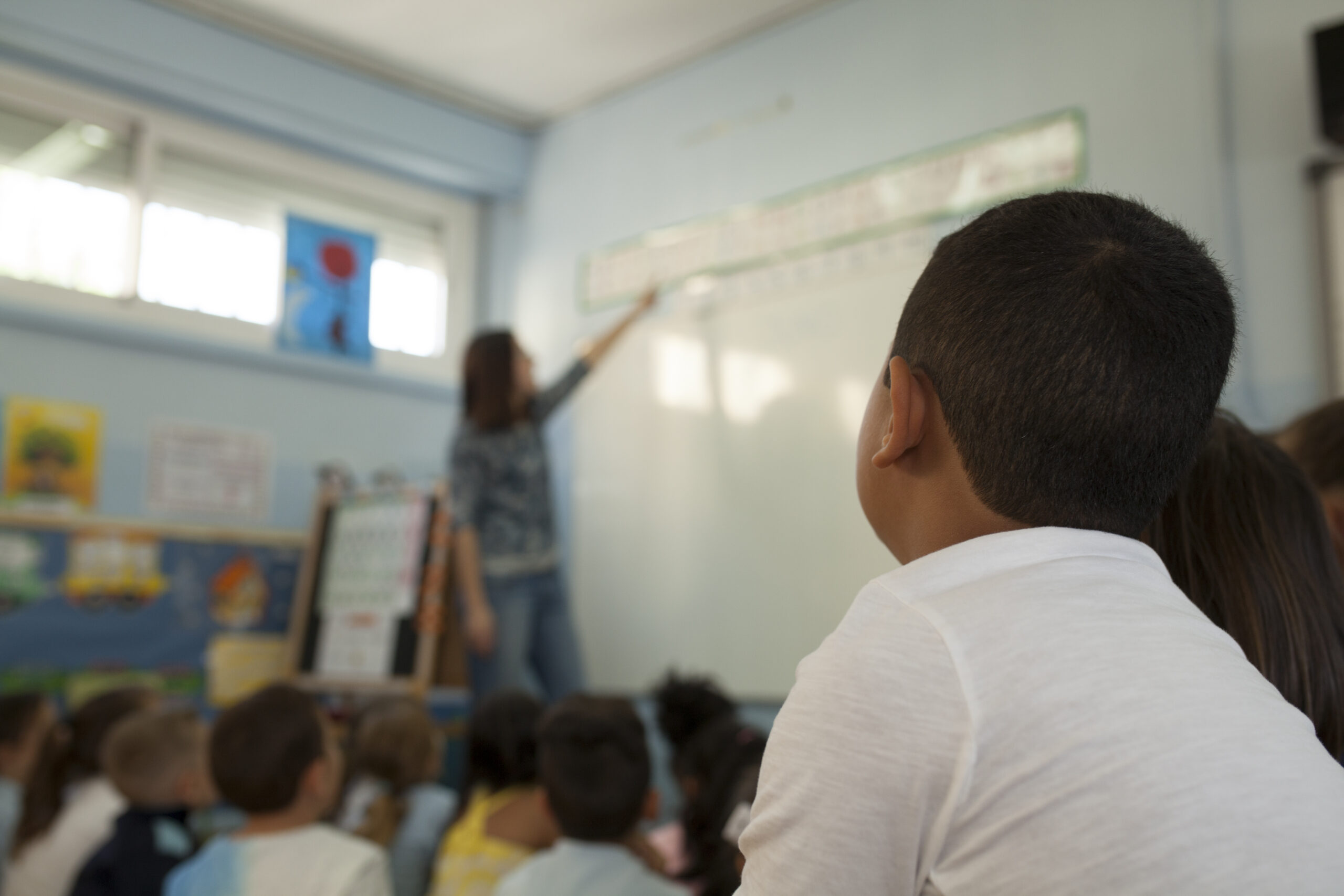 Estudiante mirando a la pizarra mientras profesora enseña.